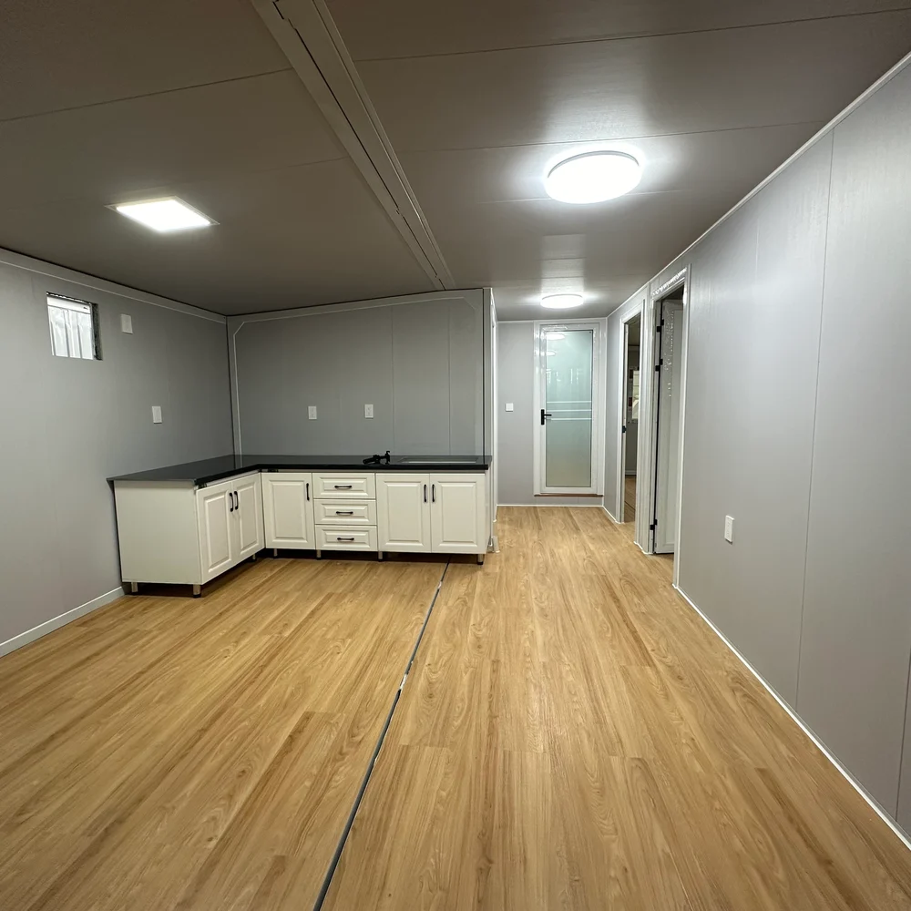 Kitchen — open floor area Open interior with corner kitchen cabinetry, warm wood-look flooring and bathroom access.
