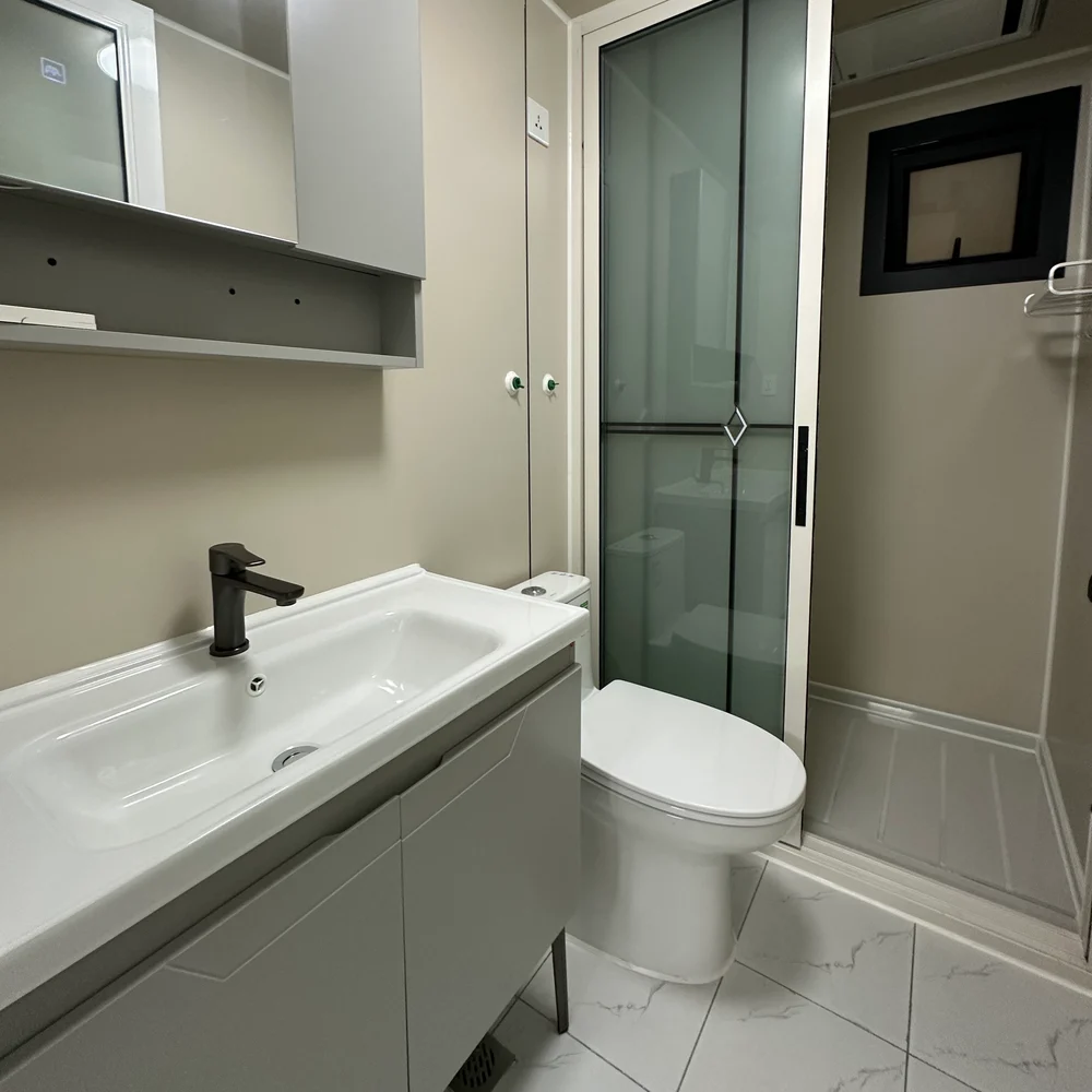 Bathroom with a grey vanity, white basin, toilet and glazed shower enclosure beside a small window.