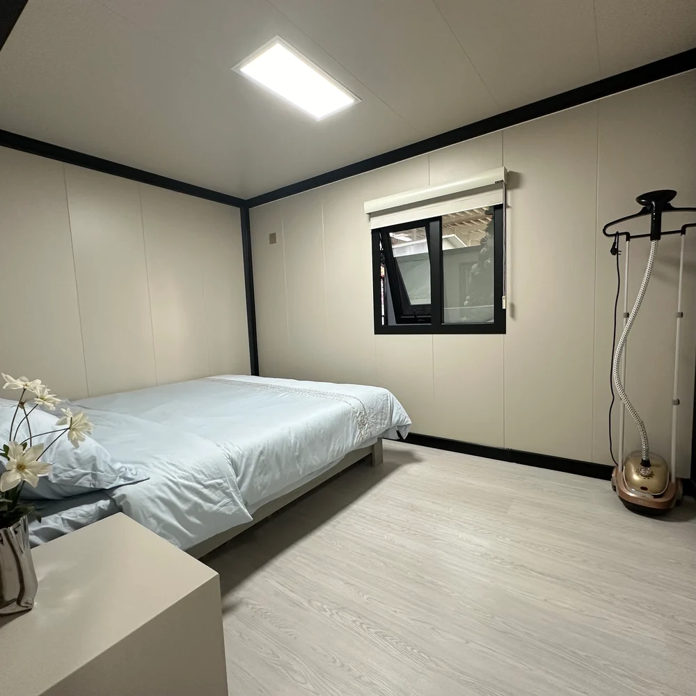 Bedroom with a bed beneath a dark-framed window and light wood-look flooring.