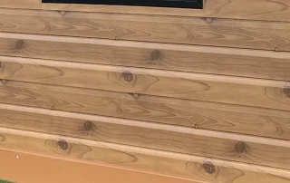 Close-up of honey-brown woodgrain metal cladding and its horizontal panel joints.