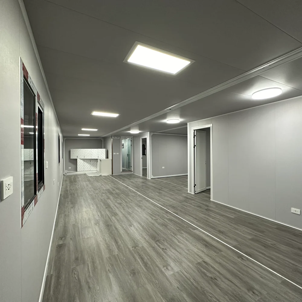 Unfurnished interior — kitchen view Open interior with grey wood-look flooring, a kitchen at the far end and doorways along one side.
