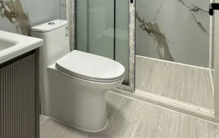 White toilet beside a bathroom vanity and marble-effect wall panels.