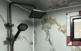 Black overhead and handheld shower fittings against marble-effect wall panels.