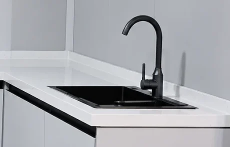Close view of the kitchen sink and curved tap set into a pale worktop above base cabinets.