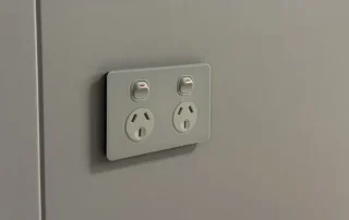 Double switched power socket mounted on a light-coloured interior wall panel.