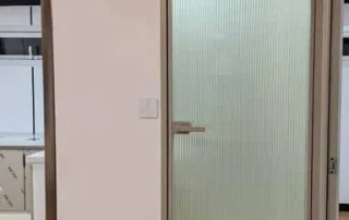 Close-up of a slim-frame bathroom door with reeded glass and a lever handle.